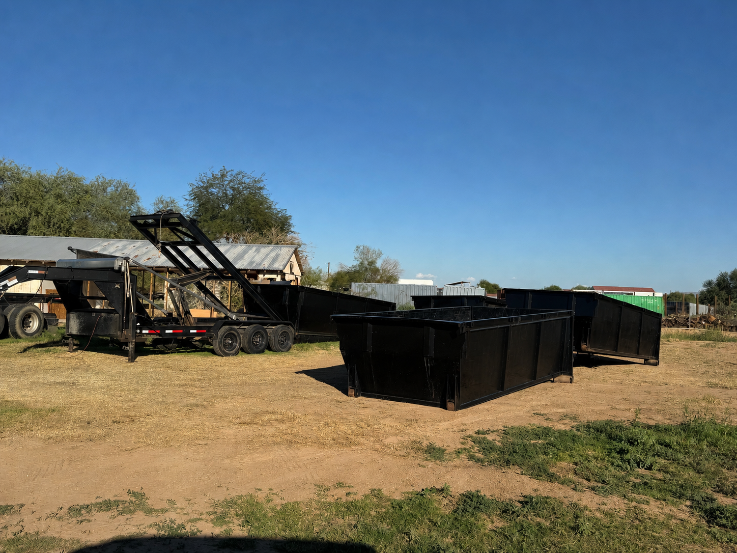 Black roll-off dumpsters and delivery trailer at a worksite